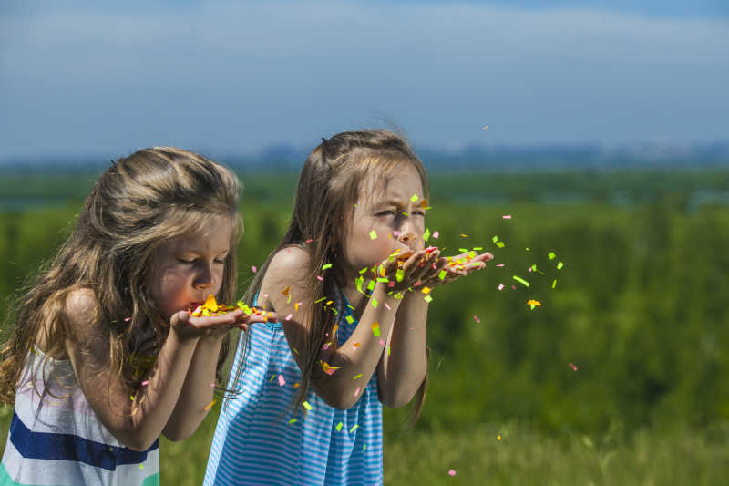 两个小女孩吹着手里的纸屑特写